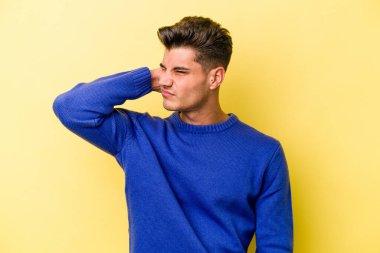 Sarı arka planda izole edilmiş genç beyaz bir adam stresten dolayı boynu ağrıyor, masaj yapıyor ve elle dokunuyor..