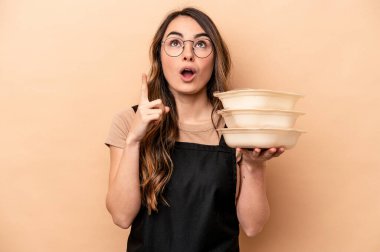 Beyaz tenli genç bir kadın bej arka planda saklanmış, ağzı açık ve üst tarafı işaret ediyor..