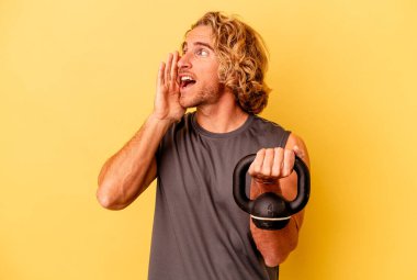 Young sport man making weightlifting isolated on yellow background shouting and holding palm near opened mouth.
