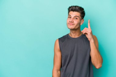 Mavi arka planda izole edilmiş genç beyaz adam bir numarayı parmağıyla gösteriyor..