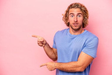 Pembe arka planda izole edilmiş genç beyaz adam işaret parmağıyla fotokopi alanını işaret ederek şok oldu..