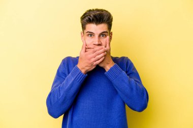 Sarı arka planda izole edilmiş genç beyaz adam elleri endişeli bir şekilde ağzı örtüyor..