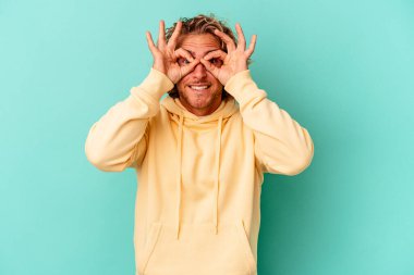 Mavi arka planda izole edilmiş genç beyaz adam gözlerinde sorun olmadığını gösteriyor.