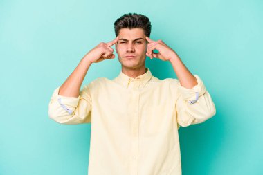 Kafkasyalı genç adam mavi arka planda izole edilmiş bir göreve odaklanmış, parmaklarını işaret ediyor..