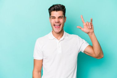 Mavi arka planda izole edilmiş genç beyaz adam boynuzlarını devrim konsepti olarak gösteriyor..