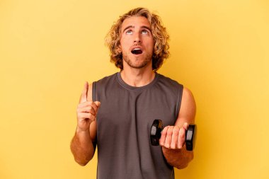 young sport man making weightlifting isolated on yellow background pointing upside with opened mouth.