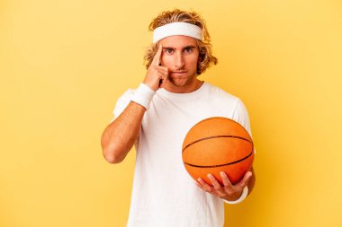 Young basketball player caucasian man isolated on yellow background pointing temple with finger, thinking, focused on a task.