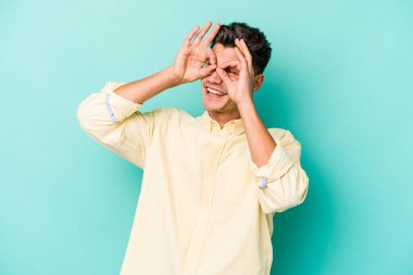 Mavi arka planda izole edilmiş genç beyaz adam gözlerinde sorun olmadığını gösteriyor.