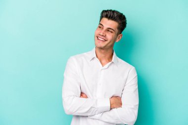 Kafkasyalı genç adam mavi arka planda izole edilmiş hedeflerine ve amaçlarına ulaşma hayali kuruyor.