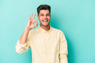 Kafkasyalı genç adam mavi arka planda izole edilmiş neşeli ve kendinden emin..