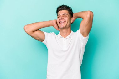 Mavi arka planda izole edilmiş genç beyaz adam kollarını uzatıyor, rahat bir konumda..
