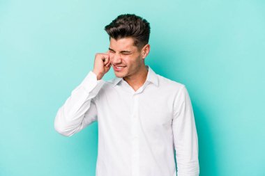 Mavi arka planda izole edilmiş genç beyaz adam kulaklarını elleriyle kapatıyor..