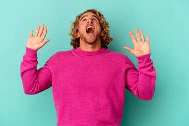 Kafkasyalı genç adam mavi arka planda izole edilmiş gökyüzüne haykırıyor, yukarı bakıyor, hayal kırıklığına uğramış..