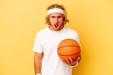 Young basketball player caucasian man isolated on yellow background screaming very angry and aggressive.