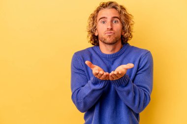 Sarı arka planda izole edilmiş genç, beyaz bir adam. Dudaklarını kıvırıyor, avuç içlerini tutuyor ve hava öpücüğü yolluyor..