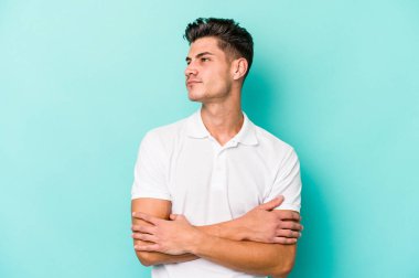 Kafkasyalı genç adam mavi arka planda izole edilmiş hedeflerine ve amaçlarına ulaşma hayali kuruyor.