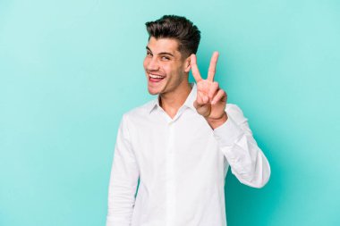 Mavi arka planda izole edilmiş genç beyaz adam iki numarayı parmaklarıyla gösteriyor..