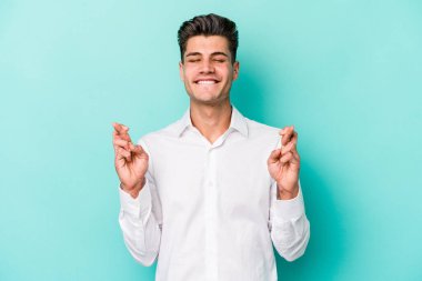 Kafkasyalı genç adam mavi arka planda izole edilmiş şans dilemek için şans diliyor.