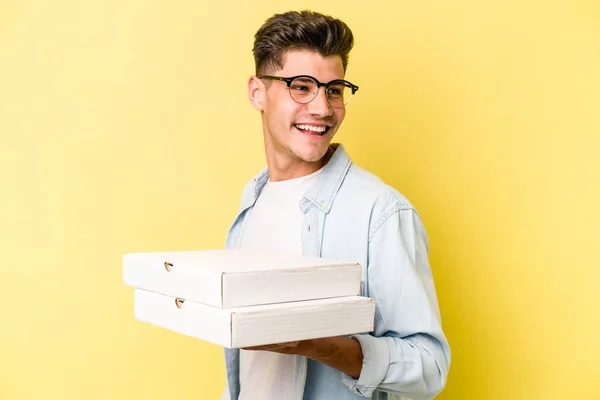 Joven Hombre Caucásico Sosteniendo Pizzas Aisladas Sobre Fondo Amarillo Mira — Foto de Stock