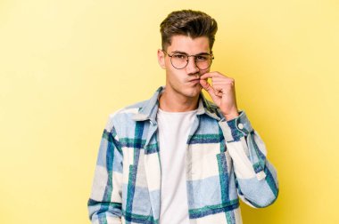 Sarı arka planda izole edilmiş genç beyaz bir adam parmakları dudaklarında bir sır saklıyor..