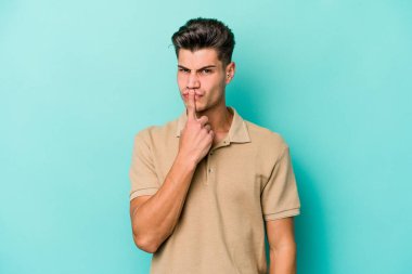 Kafkasyalı genç adam mavi arka planda izole edilmiş düşünüyor ve bakıyor, yansıtıyor, düşünüyor, bir fantezi kuruyor..