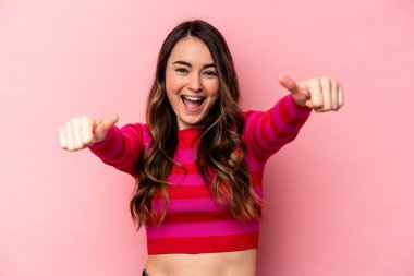 Pembe arka planda izole edilmiş genç beyaz kadın iki parmağını da kaldırıyor, gülümsüyor ve kendinden emin..