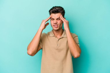 Genç beyaz adam mavi arka planda izole edilmiş tapınaklara dokunuyor ve başı ağrıyor..