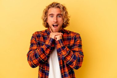 Kafkasyalı genç adam sarı arka planda izole edilmiş şans için dua ediyor, şaşırmış ve ağzını açıp önüne bakıyor..