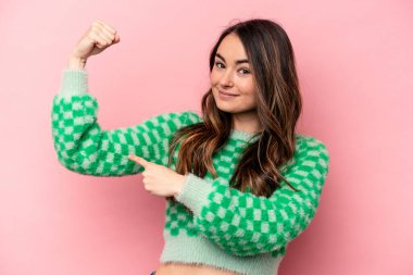 Pembe arka planda izole edilmiş genç beyaz kadın güçlü bir hareket gösteriyor. Kollarıyla, kadınsı gücün sembolü.