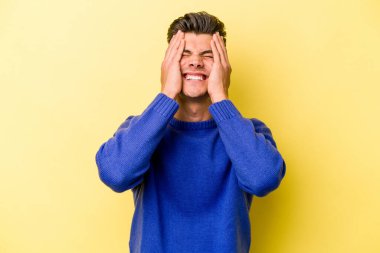 Kafkasyalı genç adam sarı arka planda izole edilmiş, ağlıyor, bir şeyden memnun değil, acı ve kafa karışıklığı kavramı..