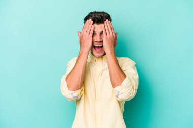 Mavi arka planda izole edilmiş genç beyaz adam yüzünün yarısını palmiye ile kaplayarak eğleniyor..