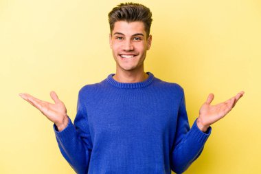 Kafkasyalı genç adam sarı arka planda izole edilmiş. Kafası karışmış ve omuz silkiyor. Kopya alanını tutmak için..