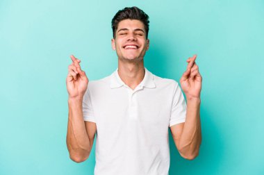 Kafkasyalı genç adam mavi arka planda izole edilmiş şans dilemek için şans diliyor.