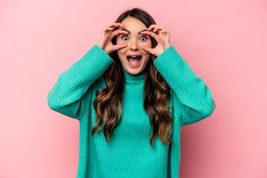 Pembe arka planda izole edilmiş genç beyaz kadın bir başarı fırsatı bulmak için gözlerini açık tutuyor..