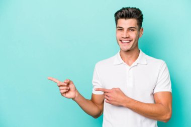 Kafkasyalı genç adam mavi arka planda izole edilmiş. İşaret parmağıyla işaret ettiği için heyecanlı..