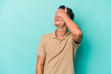 Mavi arka planda izole edilmiş genç beyaz adam ellerini başının üstünde tutarak neşe içinde gülüyor. Mutluluk kavramı.