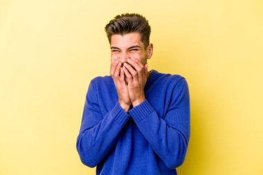 Sarı arka planda izole edilmiş genç beyaz bir adam bir şeye gülüyor, ağızlarını ellerle kapatıyor..