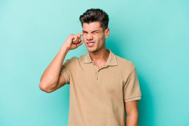 Genç beyaz adam mavi arka planda izole edilmiş parmaklarıyla kulaklarını kapatıyor, gürültülü bir ortam tarafından stresli ve umutsuz..