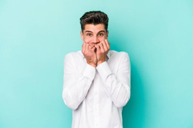 Mavi arka planda izole edilmiş, tırnak yiyen, gergin ve endişeli genç bir beyaz adam..