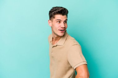 Mavi arka planda soyutlanmış genç beyaz bir adam gülümsüyor, neşeli ve keyifli görünüyor..