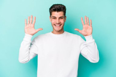 Mavi arka planda izole edilmiş genç beyaz adam on numarayı elleriyle gösteriyor..
