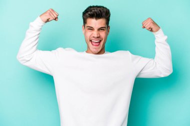 Mavi arka planda izole edilmiş genç beyaz adam güçlü bir hareket sergiliyor kollarıyla, kadınsı gücün sembolü.