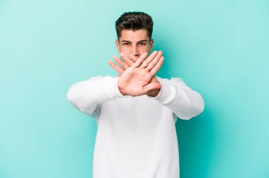 Kafkasyalı genç adam mavi arka planda izole edilmiş bir şekilde inkar hareketi yapıyor.