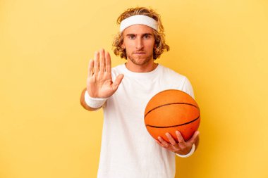 Young basketball player caucasian man isolated on yellow background standing with outstretched hand showing stop sign, preventing you.