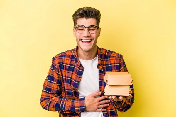 Joven Hombre Caucásico Sosteniendo Una Hamburguesa Aislada Sobre Fondo Amarillo — Foto de Stock