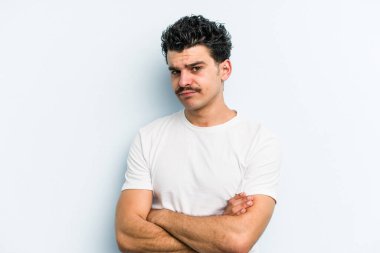 Kafkasyalı genç adam mavi arka planda izole edilmiş şüpheli, belirsiz, seni muayene ediyor..