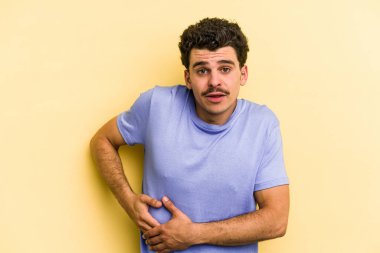 Sarı arka planda karaciğer ağrısı çeken, karnı ağrıyan genç beyaz bir adam..