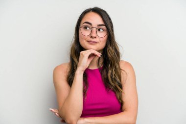 Beyaz arka planda izole edilmiş genç beyaz kadın şüpheli, belirsiz, seni muayene ediyor..