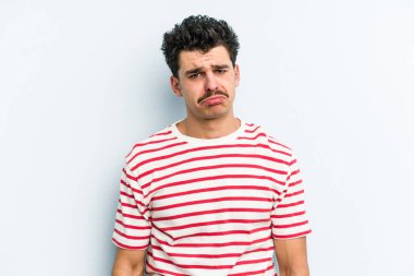 Kafkasyalı genç adam mavi arka planda izole edilmiş üzgün, ciddi yüzlü, mutsuz ve hoşnutsuz..