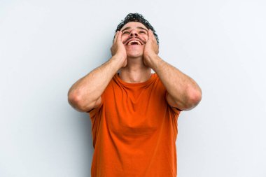 Mavi arka planda izole edilmiş genç beyaz adam ellerini başının üstünde tutarak neşe içinde gülüyor. Mutluluk kavramı.